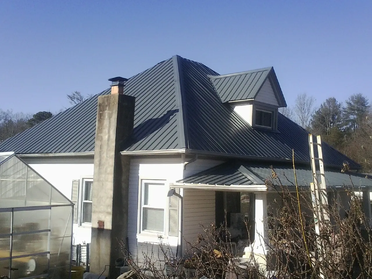 Dark blue standing seam metal roof on a white farmhouse with dormer — Slate & Tile Roof Repair by Roofing Brothers in Pingree