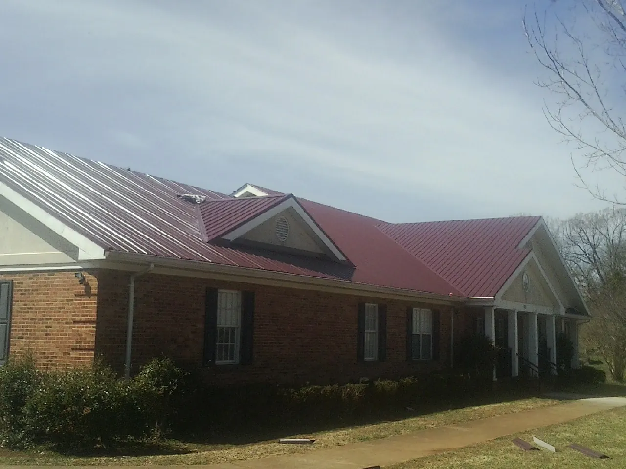Red metal roof with gabled entries on a long brick building, from a Hail Damage Roof Repair job in Pingree