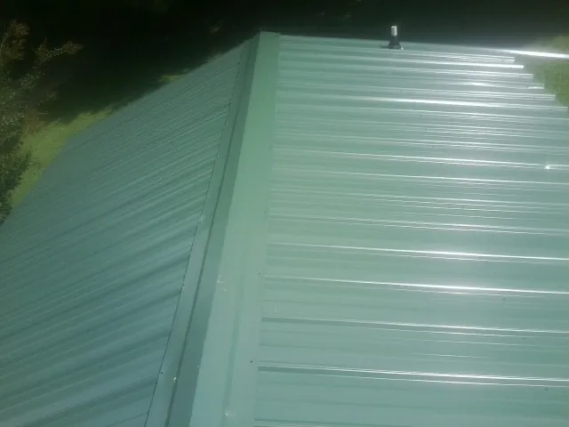 New green metal panels meeting at the ridge of a roof — Flat Roof Repair work by our crew in Pingree