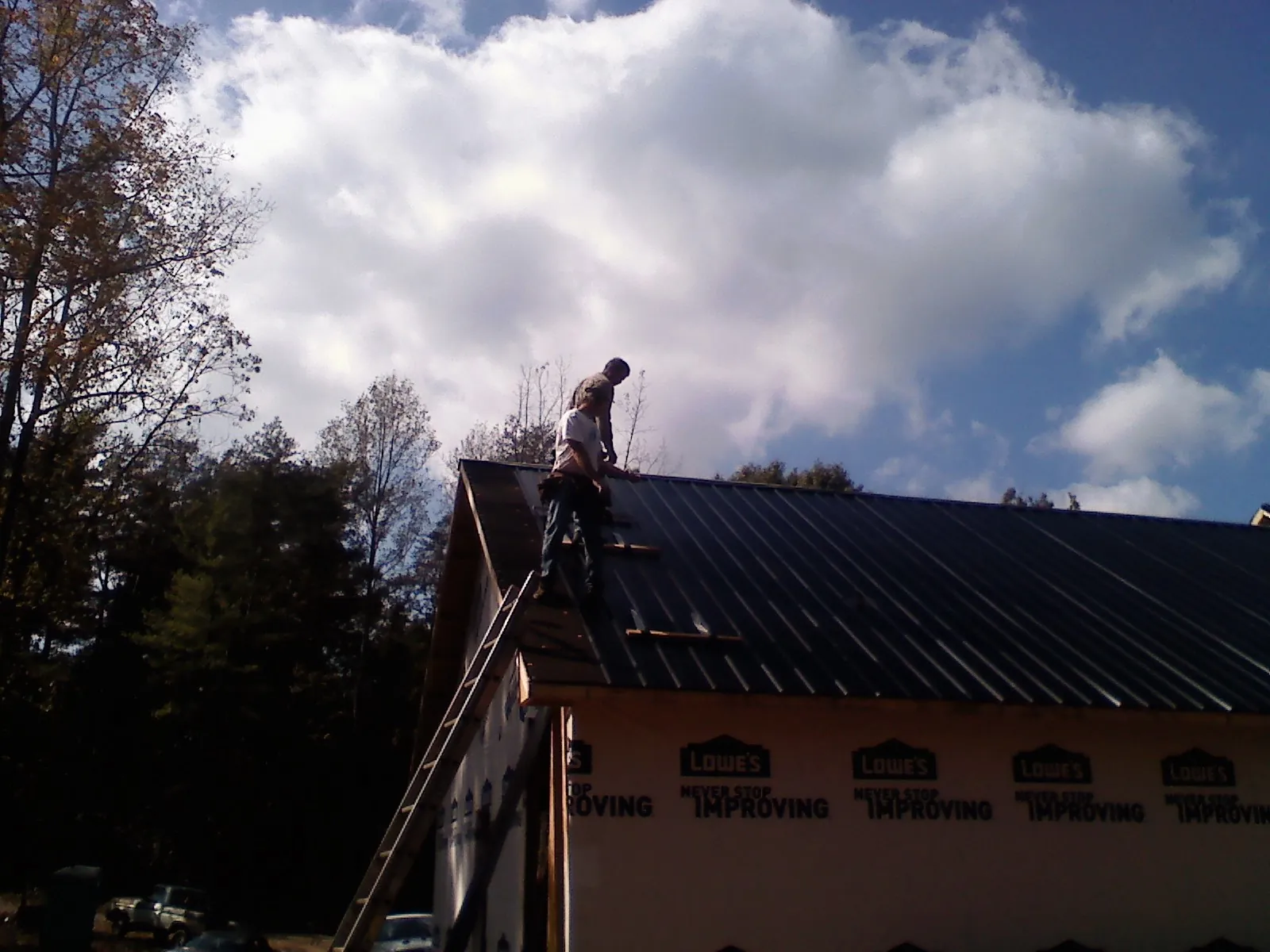 Roofer fastening dark metal panels high against a cloudy sky, from a Roof Inspection job in Pingree