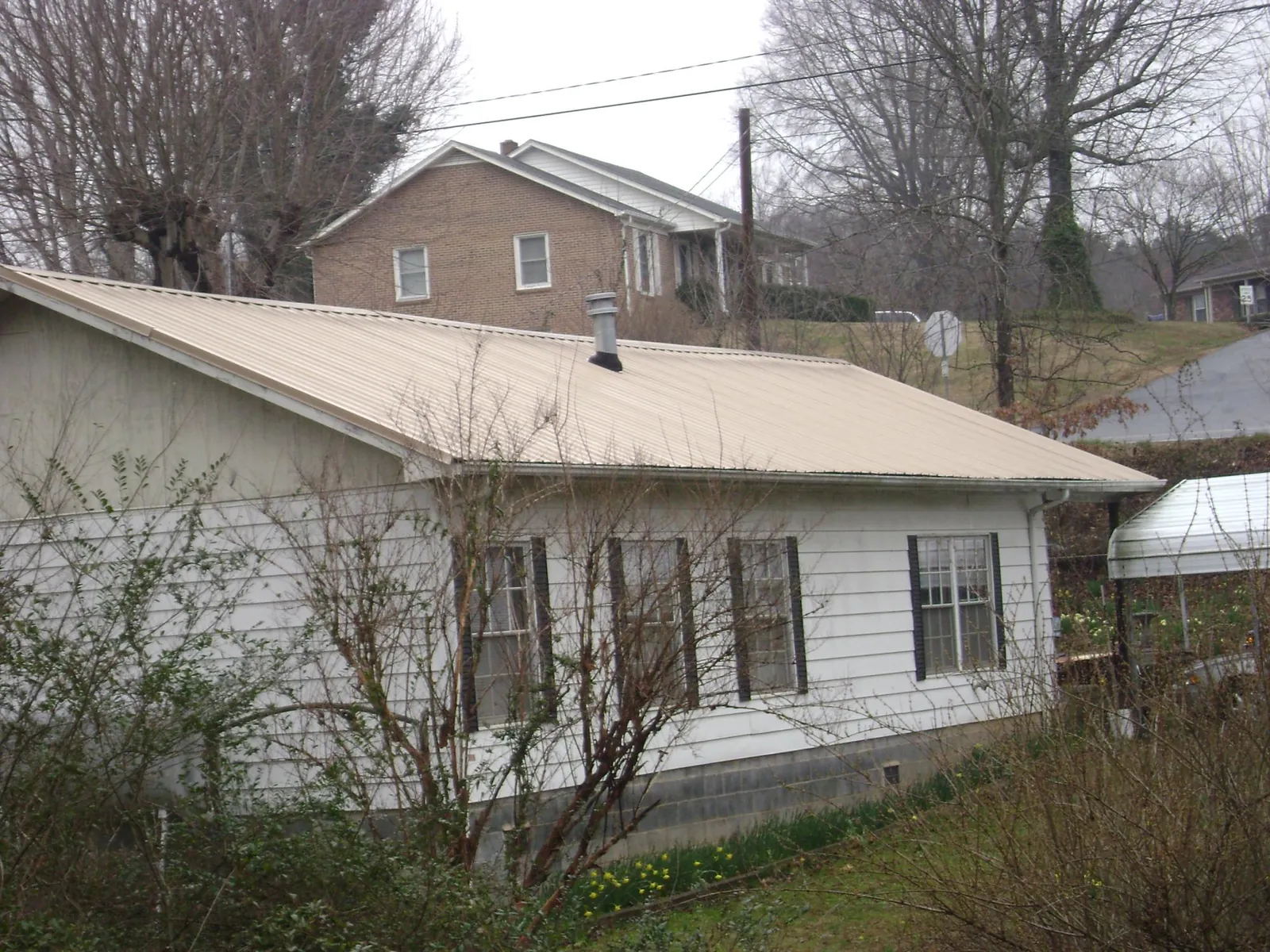 Tan metal roof on a white sided house set into a hillside — Commercial Roofing by Roofing Brothers in Pingree